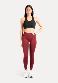 Brassière de sport noire et leggings bordeaux, coupe ajustée, taille haute avec texture lisse. Baskets blanches avec accents réfléchissants.