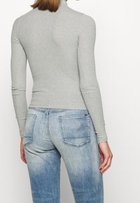 Ljusgrå långärmad topp med ribbad textur, kombinerad med bleka blå jeans i denim med bakfickor och en diskret logodetalj.