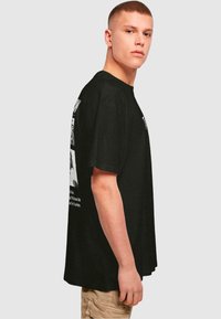 Black cotton t-shirt with a relaxed fit, featuring graphic prints on the back. The fabric appears soft with a smooth texture.
