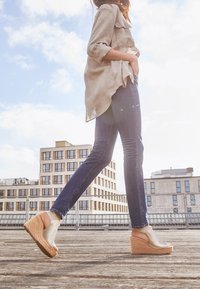 Kilklackssandaler med en beige läderöverdel och en naturlig repplattform. Modellen har på sig blå jeans och en ljusbeige oversized skjorta.