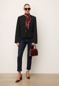 Svart kort blazer med stora knappar, tillsammans med mörka jeans, bourgognefärgade högklackade skor, en mönstrad bourgognefärgad scarf och en liten handväska.