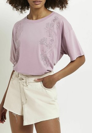 Różowy t-shirt z krótkim rękawem, ozdobiony kwiatowym haftem z przodu, zestawiony z jasnobeżową spódnicą dżinsową z surowym wykończeniem i przednią kieszenią.