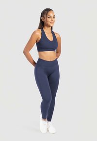 Marineblå sportbehå och leggings i ribbat tyg med en figursydd design. Matchas med vita träningsskor.