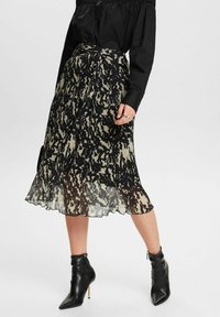 Falda plisada negra y topo con un dobladillo ondulado y un patrón abstracto, combinada con botas de tobillo puntiagudas negras con un acento dorado.