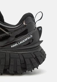Talons épais noirs de baskets avec semelle à gros crampons, col rembourré et logo blanc Karl Lagerfeld sur le panneau latéral.