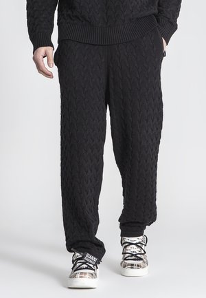 Pantalones de punto trenzado negros con un corte relajado y cinturilla elástica. Combinados con zapatillas distintivas de patrón en blanco y negro.