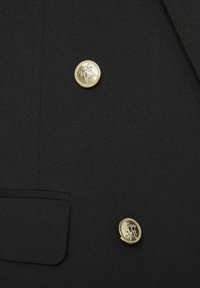 Blazer noir avec deux boutons décoratifs dorés brillants et un rabat de poche sur le côté gauche.