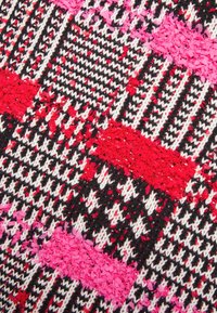 Gros plan d’un tissu tricoté avec des motifs géométriques rouges, roses, noirs et blancs et des détails de fil texturé.