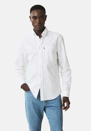 Hvid langærmet skjorte i let bomuld med knapkrave og brystlomme, parret med lyseblå denimjeans.