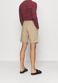 Beiga shorts med avslappnad passform, kombinerade med en texturerad långärmad skjorta i mörkröd färg. Svarta sandaler fulländar outfiten.