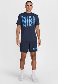 Navy blue athletic t-shirt with large light blue "NIKE" graphic, paired with matching navy shorts featuring a smaller logo, both made of breathable fabric.
