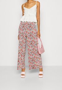 Haut peplum blanc avec bretelles ajustables, associé à un pantalon large floral dans des teintes de rose, vert et orange. Accessoires comprenant un sac à main rose et des talons.