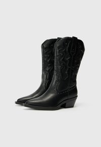 Botas vaqueras de cuero negro con puntas afiladas, costuras decorativas texturizadas, tachuelas metálicas a lo largo de las costuras y un tacón bajo apilado.