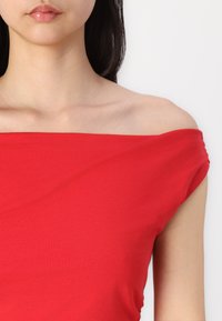 Red off-the-shoulder top made of lightweight fabric with a smooth texture. This design features a draped neckline and fitted silhouette.