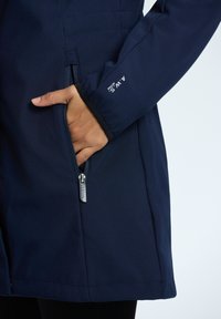 Giacca blu navy con tasca con zip e dettaglio del logo sulla manica, realizzata in tessuto liscio con una leggera texture.