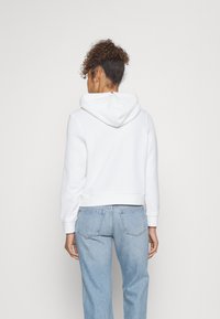 Felpa bianca corta con cappuccio regolabile e polsini a costine, abbinata a jeans a vita alta azzurri chiari con tasche posteriori.