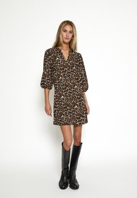Šaty s leopardím vzorom, vybavené 3/4 balónovými rukávmi, V-výstrihom a voľným strihom, doplnené čiernymi koženými čižmami po kolená.