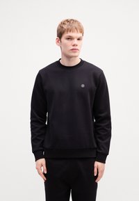 Sort sweatshirt lavet af blødt, tykt stof. Har en rund halsudskæring, ribbede manchetter og kant, samt et lille logo på brystet.