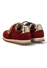 Par de zapatillas de ante rojo con acentos dorados en el talón, suelas de goma y cordones en beige y azul marino contrastantes, mostradas desde la parte trasera.