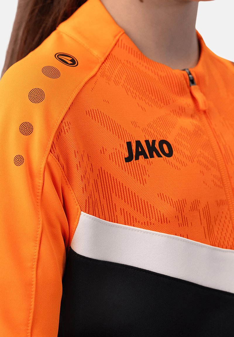 Giacca sportiva arancione con chiusura a zip, tessuto testurizzato, lettering nero, striscia bianca e design ad accento puntinato sulla spalla.