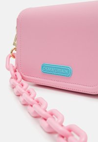 Pink rectangular purse with chunky pink plastic chain strap and blue "Chiara Ferragni" logo patch on front.