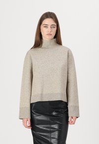 Beige strikkegenser med høy krage, avslappet passform og vide ermer; kombinert med et svart strukturert skjørt med krokodillemønster.