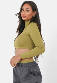 Olijfgroen geribbelde lange mouwen cropped top met een opstaand kraag, gecombineerd met grijze jogpants met trekkoord. Soepele textuur, aansluitend ontwerp.