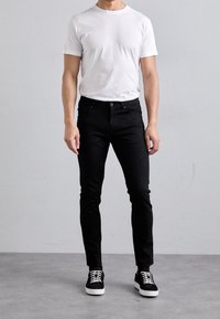 Svarta jeans i denim, tight passform, tillsammans med en enkel vit t-shirt i bomull. Svarta sneakers med vita snöre. Enfärgade, minimala detaljer.