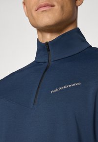 Mannen marineblauwe kwart-rits pullover met een soepele textuur, voorzien van een zwarte rits en geborduurd "Peak Performance" logo op de borst.