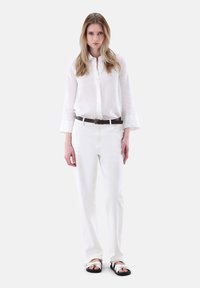 White linen shirt with long sleeves, paired with white trousers, complemented by a dark brown belt and black sandals with white straps.