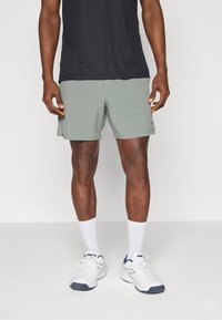 Calções atléticos verde-claro com uma cintura elástica, textura suave, bolsos laterais, combinados com sapatilhas brancas e meias de comprimento até ao tornozelo.