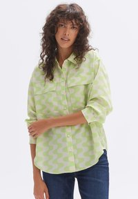 Green patterned shirt with a loose fit, featuring two chest pockets, a button-down front, and rolled-up sleeves. Soft, lightweight fabric.