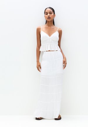 Outfit bianco a due pezzi composto da un reggiseno aderente con orlo arricciato e una lunga gonna con texture a strati e dettagli in pizzo.
