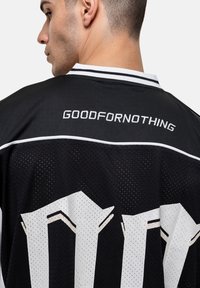 Zwart sportjersey met witte accenten, met de tekst "GOODFORNOTHING" geborduurd op de bovenrug. Mesh textuur.