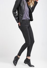 Giacca di pelle nera, maglietta grigia e jeans skinny neri abbinati a stivaletti neri alla caviglia. Texture liscia, design aderente e dettagli con punta affusolata.