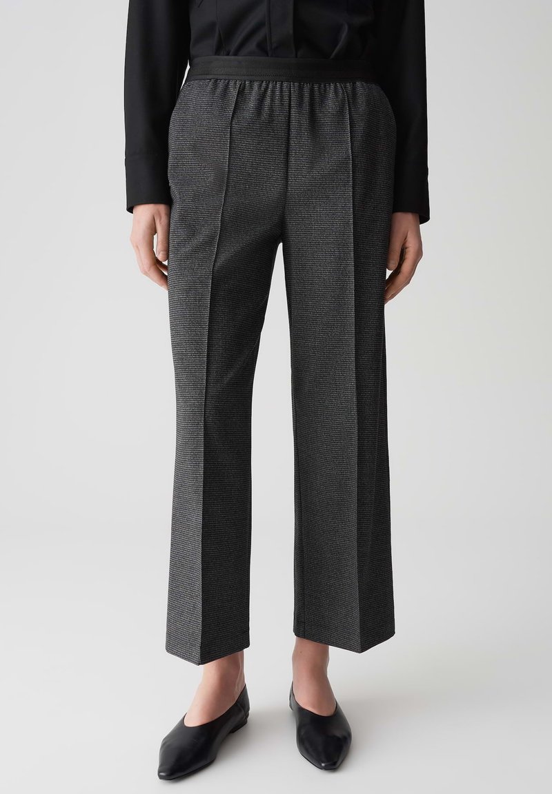 Grijze op maat gemaakte broeken met een textuurpatroon, wide-leg ontwerp, elastische tailleband en een paar zwarte instap schoenen.