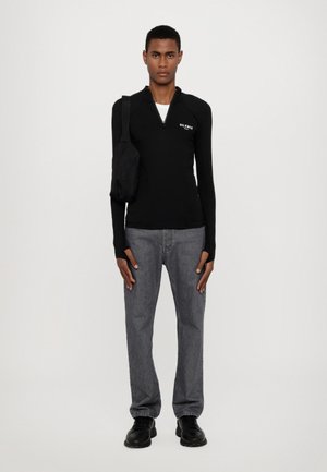 Svart langermet zip-top med "SILENCE" logo, kombinert med grå denim jeans og svarte sko, bæres med en liten svart veske.