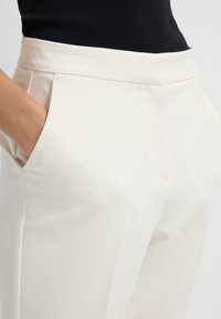 White tailored trousers made of smooth fabric with side pockets and a flat front design. Features a fitted waistband and clean lines.