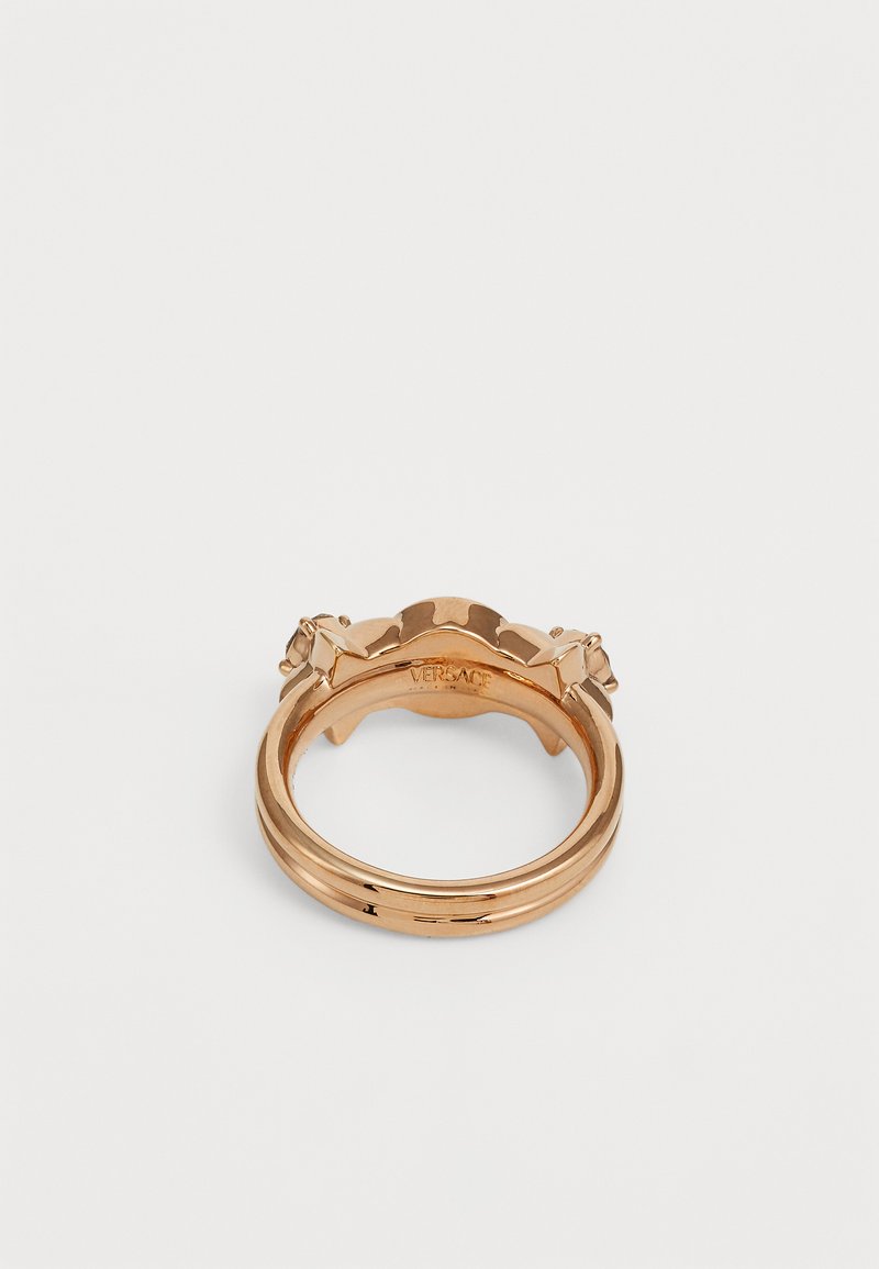 Anello in metallo color oro con design arrotondato, accenti floreali e marchio inciso all'interno. Superficie liscia e lucida.