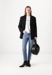 Blazer nero sartoriale sopra una maglietta bianca con grafica, abbinato a jeans a gamba dritta azzurri chiari e stivaletti neri con tacco. Borsa nera.