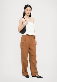 Weißes plissiertes Tanktop, braune Cargo-Hosen mit Seitentaschen, schwarze strukturierte Handtasche und spitze schwarze Schuhe. Einfaches, modernes Design.