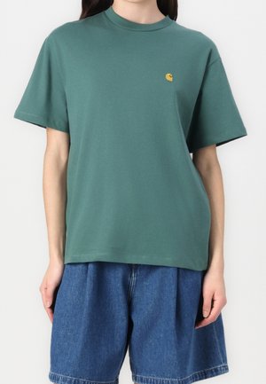 Zielona bawełniana koszulka z okrągłym dekoltem, krótkimi rękawami i małym żółtym logo na piersi. W połączeniu z niebieskimi szortami jeansowymi.