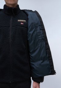 Giacca in pile nera con chiusura con zip esterna, caratterizzata da una texture morbida, logo ricamato e fodera blu navy a contrasto.