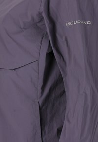 Gros plan d'un tissu violet avec le mot "ENDURANCE" imprimé en blanc dans le coin supérieur droit, montrant les plis et les détails de couture.