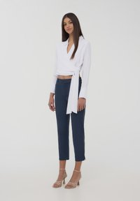 Blusa bianca avvolgente con colletto e dettaglio con fiocco, abbinata a pantaloni cropped blu navy e sandali con tacco block strappy beige.
