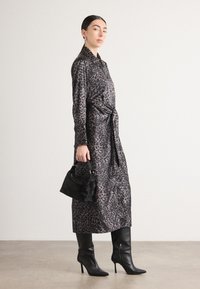 Abito lungo in tessuto seta con stampa leopardata, cinteo in vita. Abbinato a stivali neri in pelle con punta affusolata e un piccolo handbag nero.