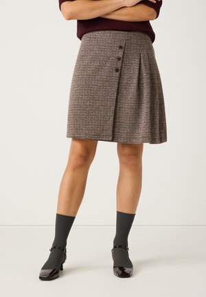 Jupe à carreaux grise avec un devant plissé, ornée de trois boutons foncés sur le côté, accompagnée de chaussettes grises et de chaussures à talons brillantes.