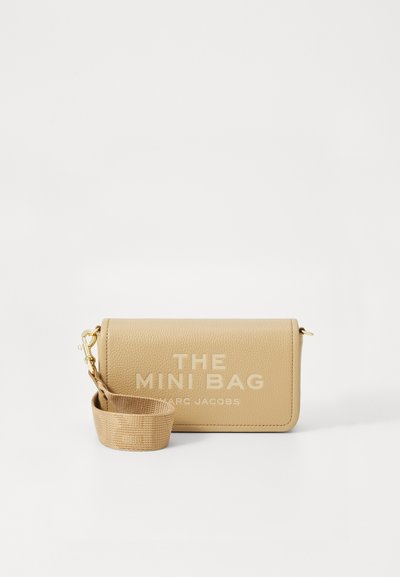 Sac beige compact en cuir texturé, arborant un imprimé logo et une bandoulière tissée amovible. Fermeture avec accent en métal.
