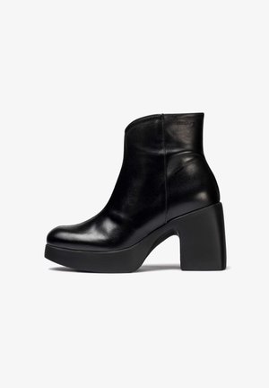 Botín negro de cuero hasta el tobillo con una textura suave, punta redondeada y un tacón de plataforma grueso. Presenta un marcado mínimo en relieve en un lado.