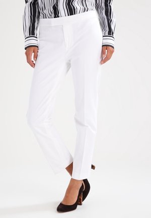 Vrouw draagt witte op maat gemaakte broek, zwart-wit gestreepte blouse met verticale strepen en zwarte hoge hakken met schildpadprint detail.